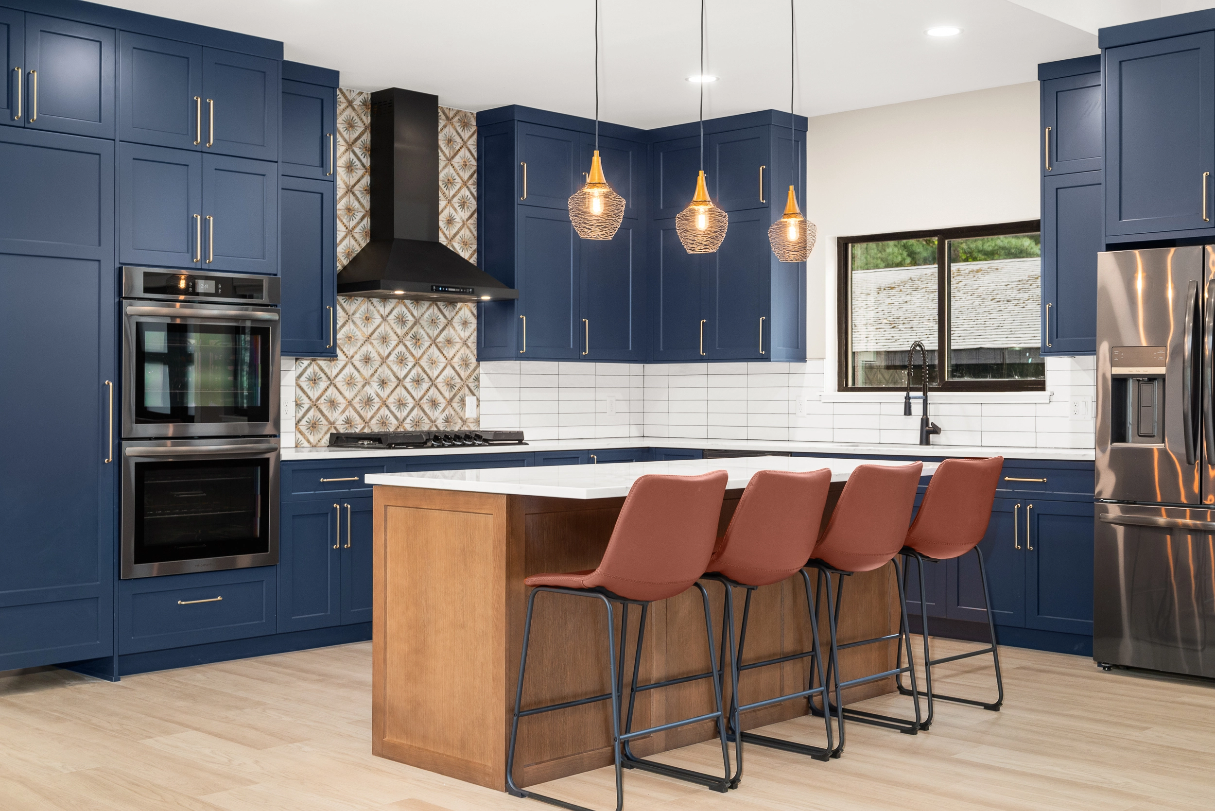 Contemporary kitchen with navy blue cabinets, white countertops, and a wooden island with burnt-orange bar stools under pendant lights.