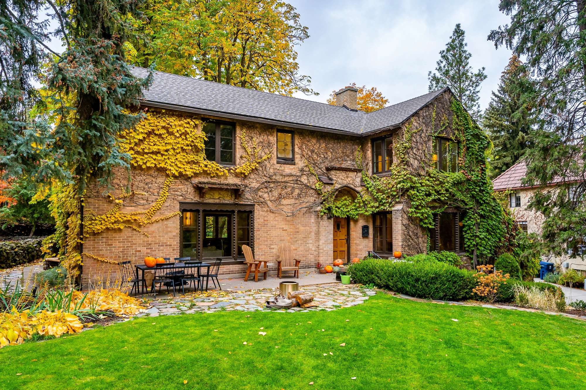 Historic brick home with ivy-covered exterior, arched entry, patio seating, landscaped yard, and mature trees in fall colors.