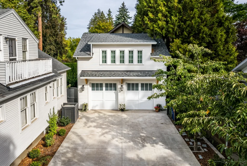 Detached two-car garage with white siding, gray shingle roof, and landscaped driveway on a residential property.