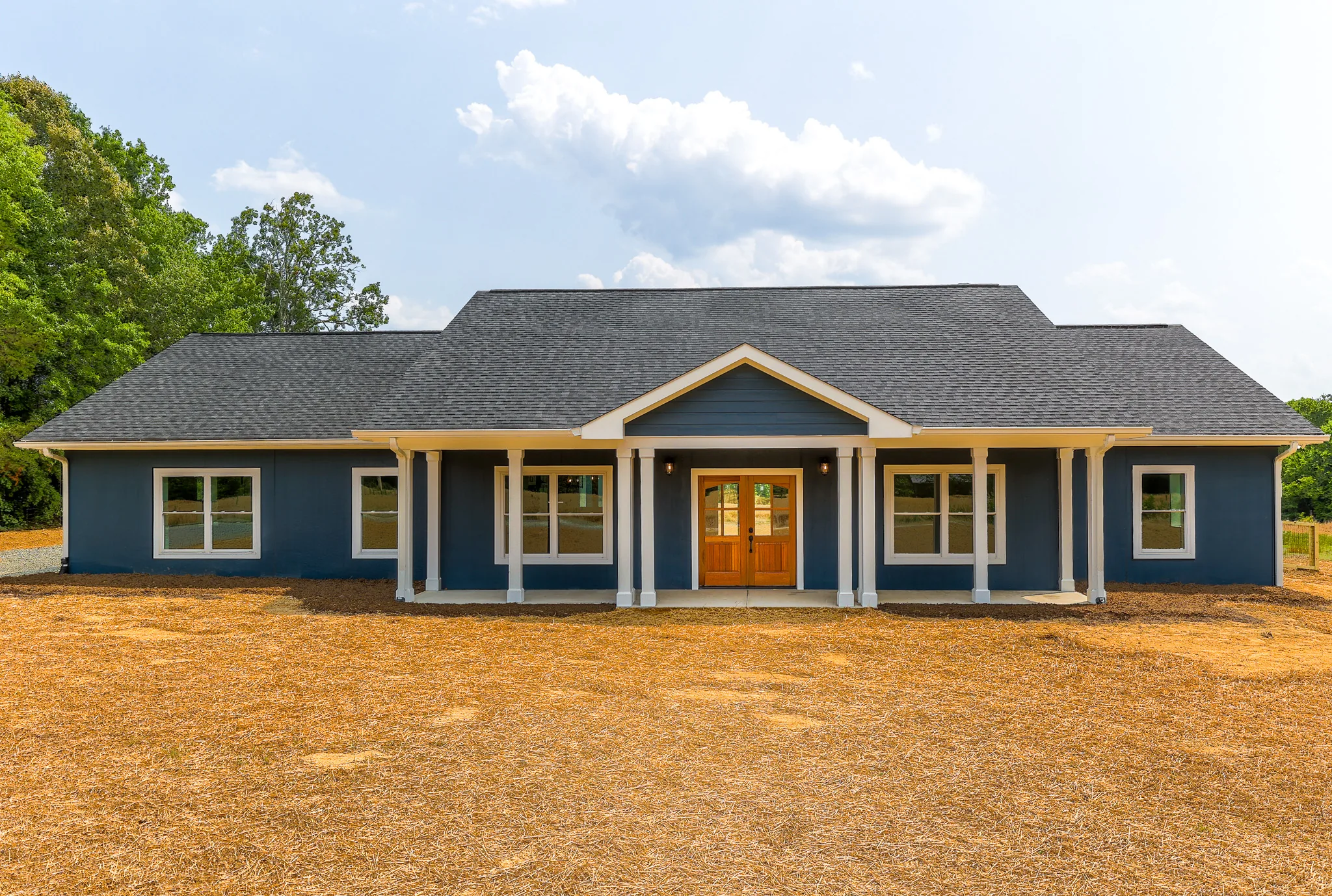 Front elevation of the Blue Juniper custom home with deep blue siding and a wood double door