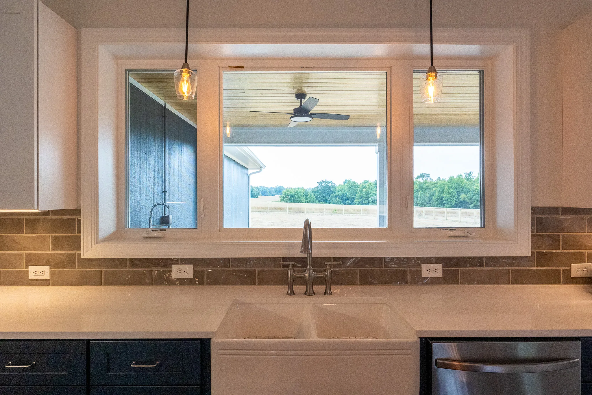 Blue-Juniper-004 | Hug Construction Farmhouse sink beneath a wide window with glass pendant lights and tile backsplash